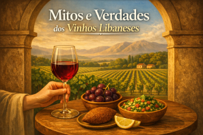 Fotografia de um cenário de vinhedo libanês visto através de arcos de pedra, com montanhas ao fundo sob um céu claro. Em primeiro plano, há uma mesa de madeira com uma taça de vinho tinto sendo segurada por uma mão, um prato de uvas roxas, um kibbeh dourado, uma tigela de salada tabule e fatias de limão. No topo da imagem, aparece o título “Mitos e Verdades dos Vinhos Libaneses”, sugerindo uma relação entre a cultura gastronômica e a tradição vinícola do Líbano.