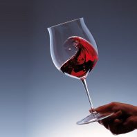 Taça de vinho tinto em movimento destacando os benefícios do vinho e a experiência sensorial. A Majestade dos Vinhos.
